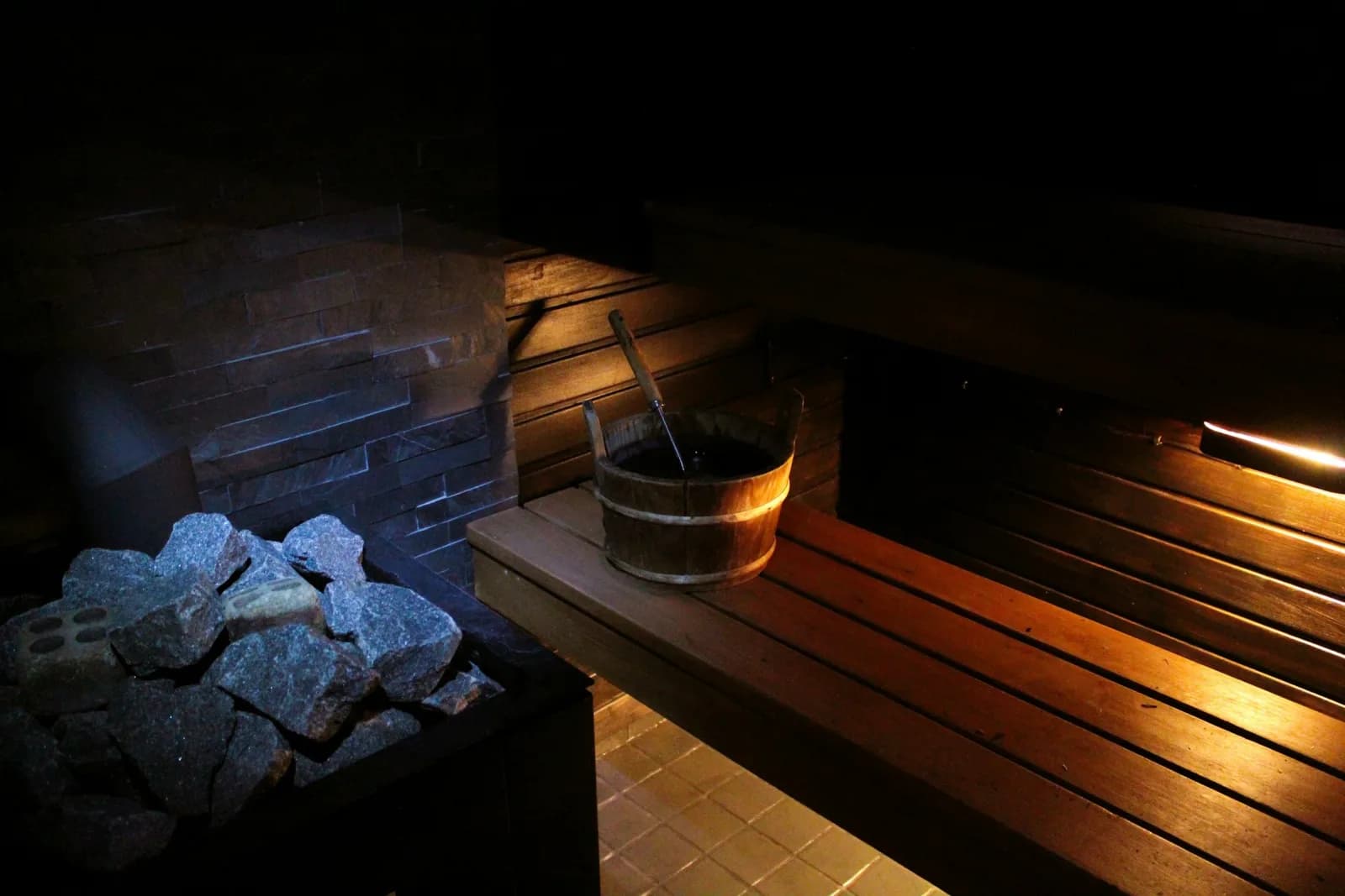 A warmly lit cedar sauna interior with stone heater and wooden water bucket — placeholder until Devon's photo is ready